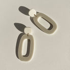 A pair of ivory beige acrylic dangle earrings on a white surface, each an open oval hung from a small rounded top on a gold-tone ring.