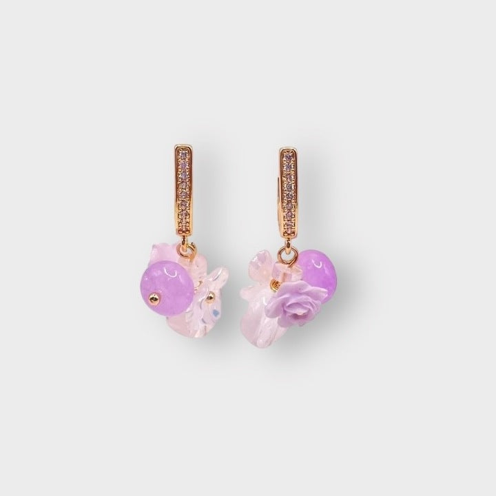 Rosarium grape earrings in Mauve: gold pavé huggie hoops hung with lilac beads, pale pink glass flowers and a lilac rose, on a pale grey background.