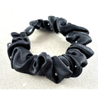 Black satin scrunchie scattered with small clear crystals, on a pale stone surface
