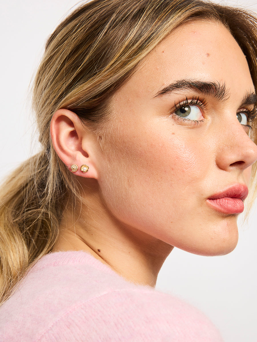 Model with her hair in a ponytail wearing a gold-tone spiral shell stud and a scallop shell stud with a pearl-look bead