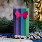 Cool and Clear gift box in purple, blue and green stripes with a pink bow, standing in front of pine branches.