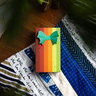 The striped Warm and Bright gift box lying on a blue and white quilt.