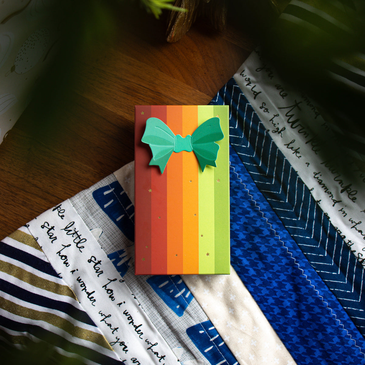The striped Warm and Bright gift box lying on a blue and white quilt.