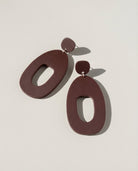 A pair of large merlot acrylic statement earrings, each a wide open shape hung from a small rounded top.