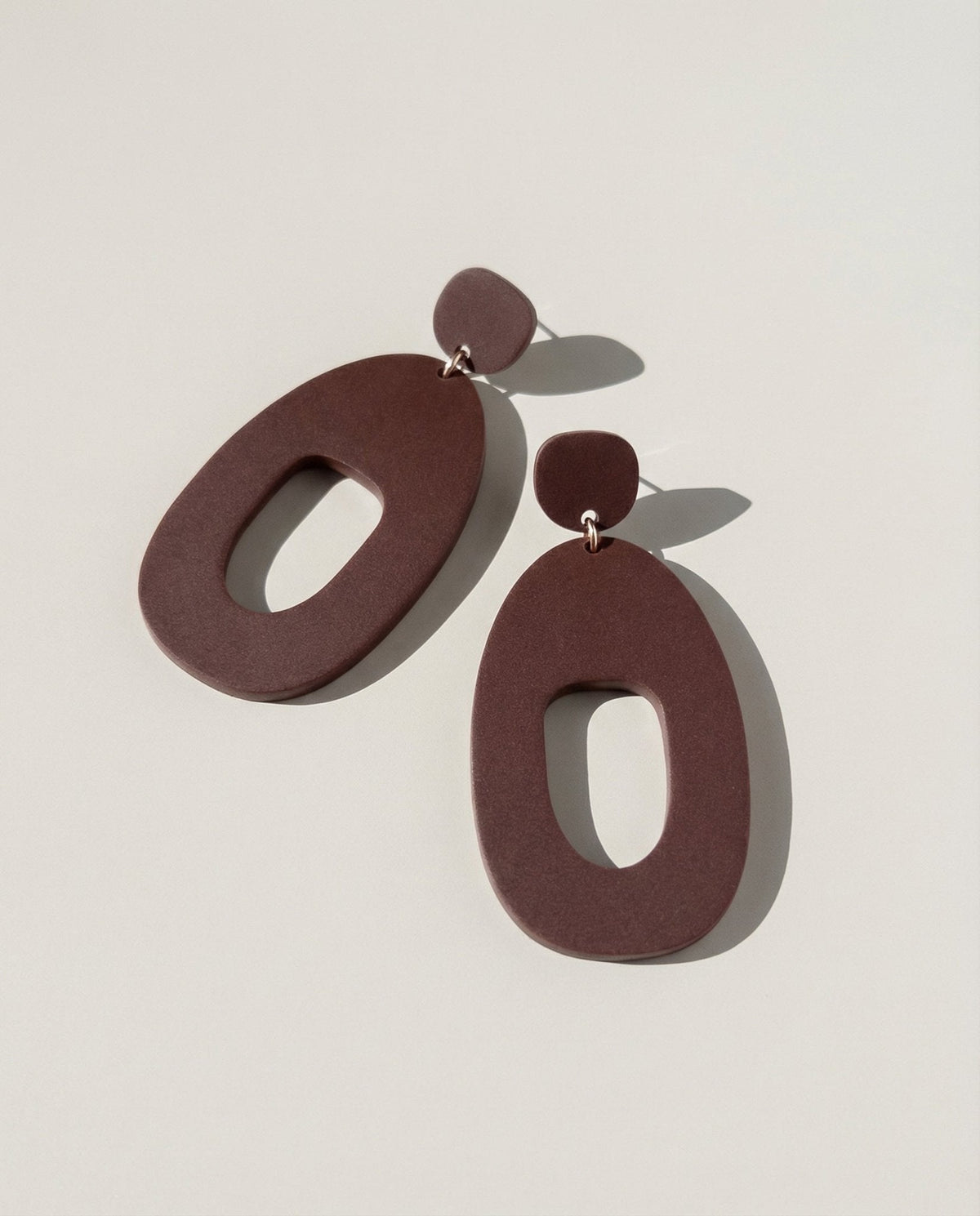 A pair of large merlot acrylic statement earrings, each a wide open shape hung from a small rounded top.
