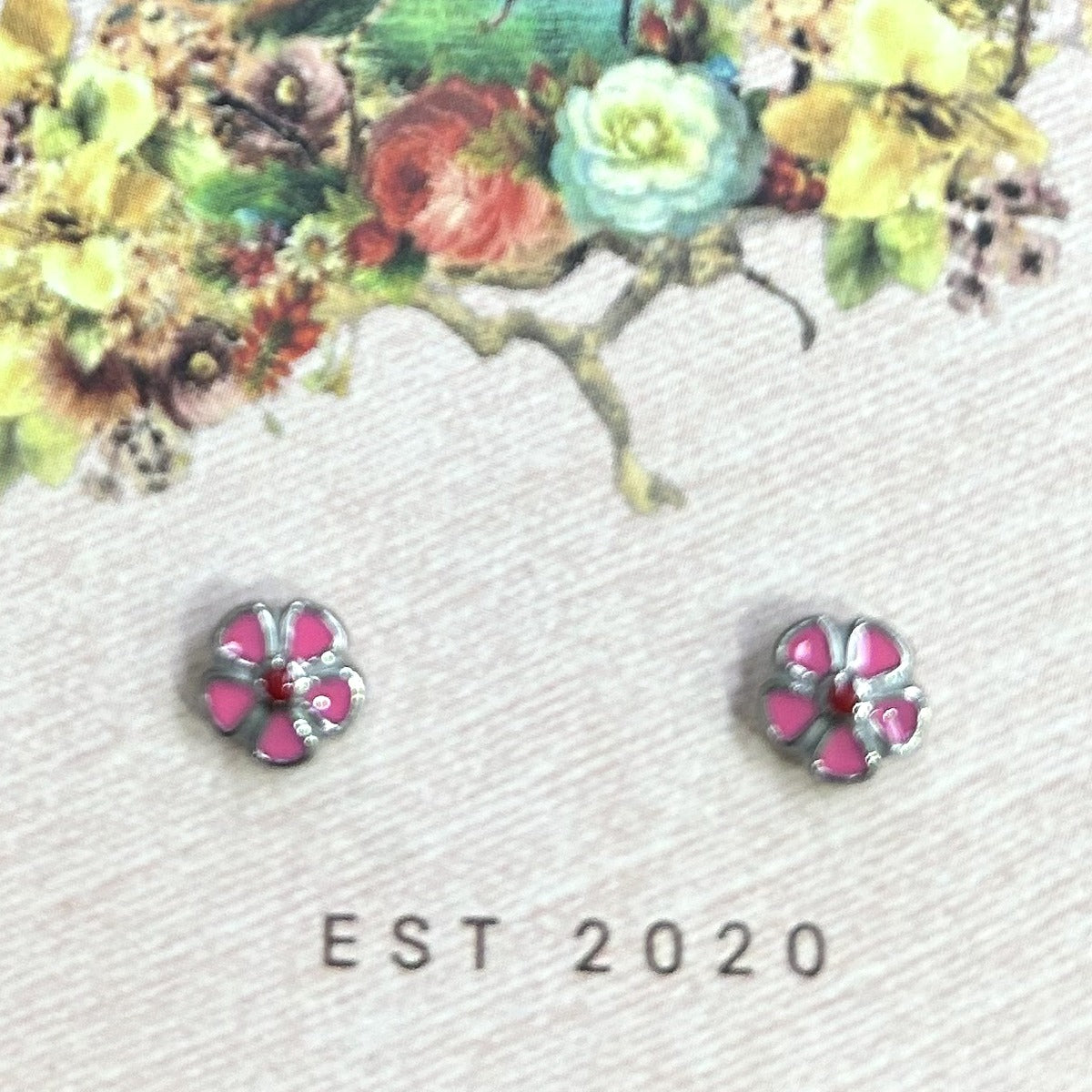 Silver-tone pink five-petal flower stud earrings with a red centre on a pink card