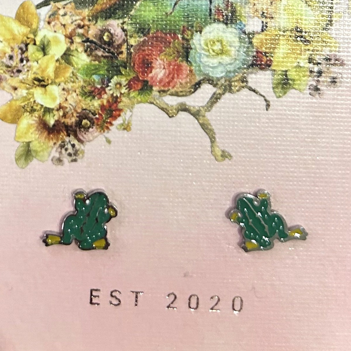 Silver-tone green frog stud earrings with yellow feet and legs out, on a pink Songbird and the Bee card