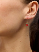 A red enamel strawberry drop earring worn on the ear.