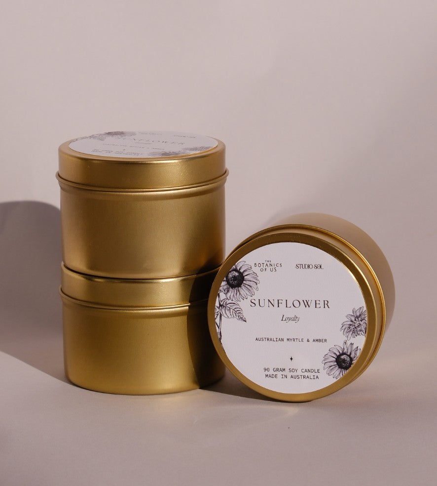 Three gold Sunflower travel tins, one tipped forward to show its lid label with a drawing of the sunflower.