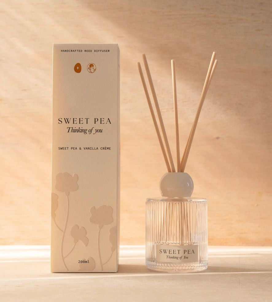 The Sweet Pea reed diffuser, a ribbed glass bottle with natural reeds, beside its cream box.