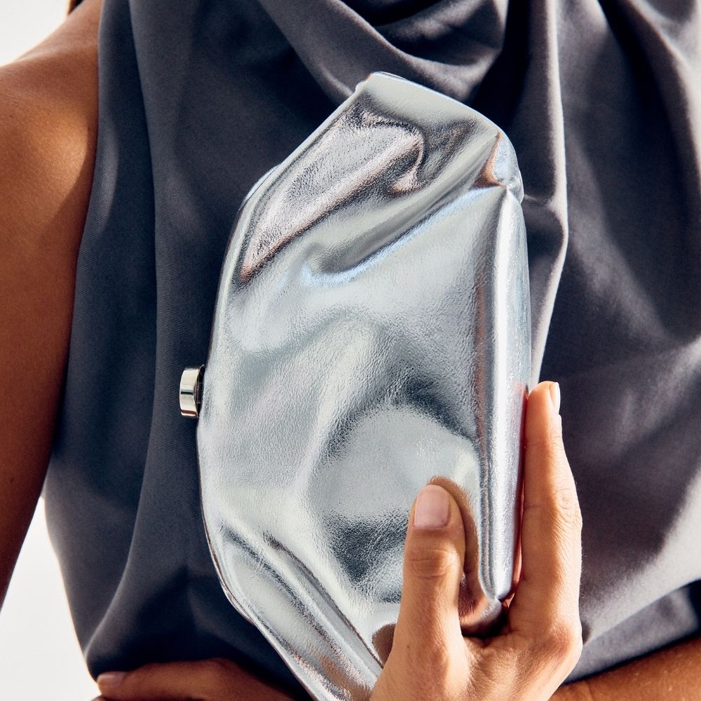 Close-up of a hand holding the soft silver clutch against navy fabric