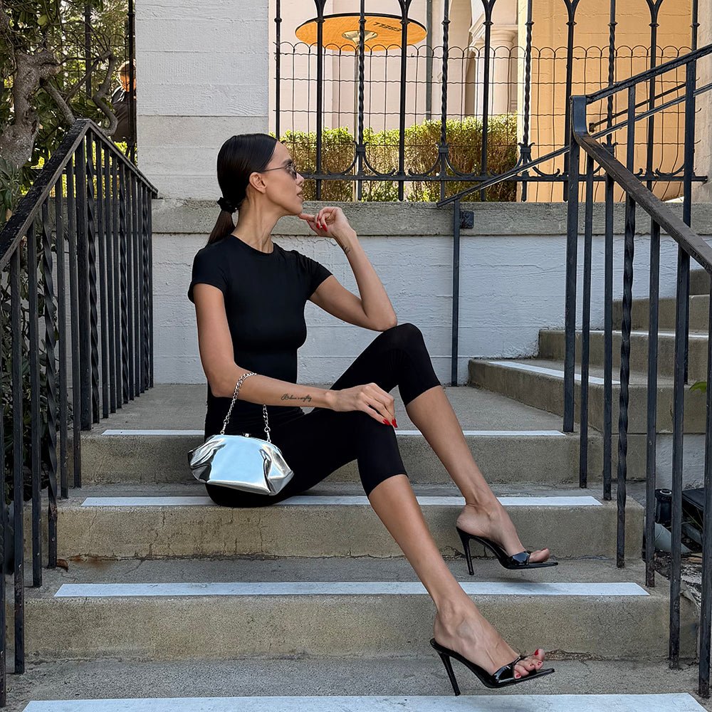 Woman in black sitting on stone steps, holding the silver clutch at her knee