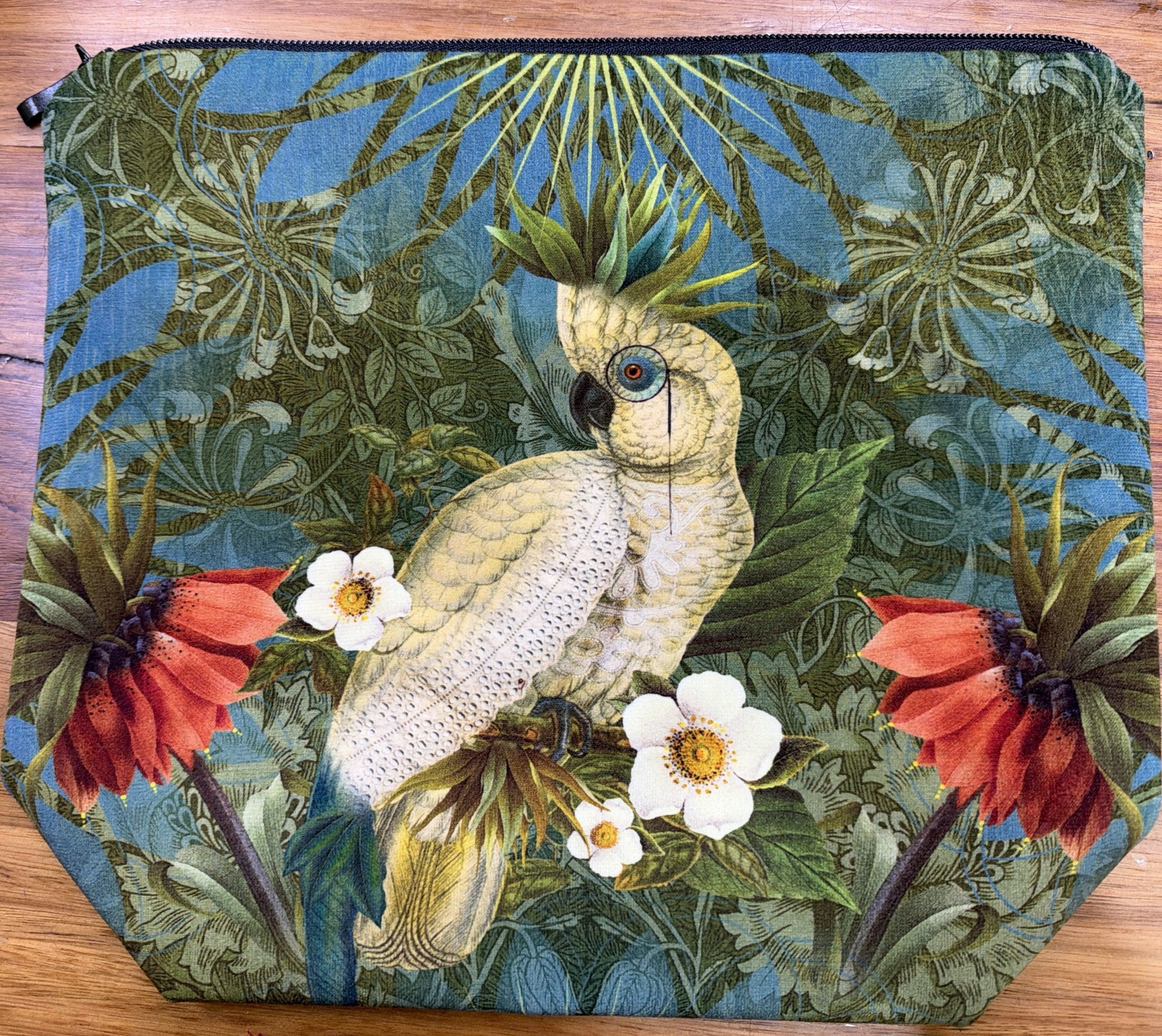 Velour cosmetic bag printed with Isabelle Frioux's Parrot with Glasses: a white cockatoo wearing a monocle among red and white flowers, with a black zip.