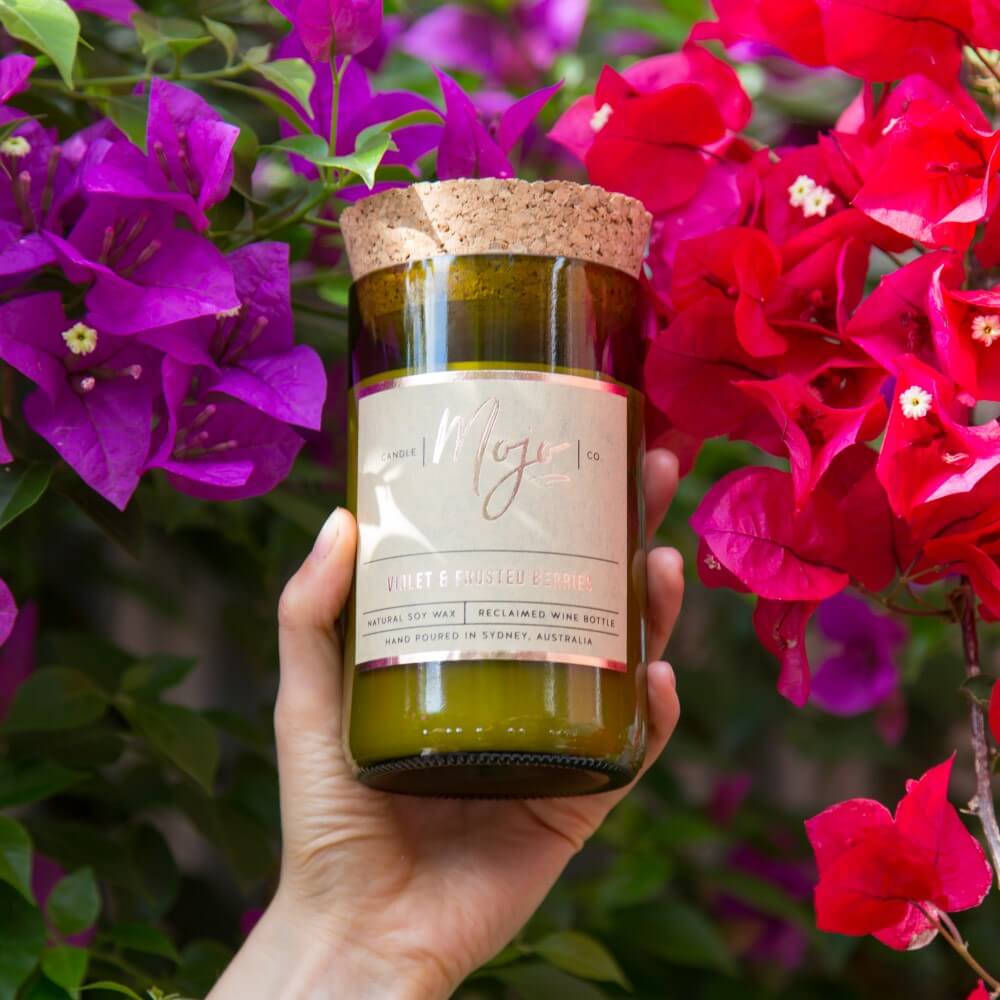 Hand holding the Violet & Frosted Berries candle in front of pink bougainvillea