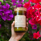 Hand holding the Violet & Frosted Berries candle in front of pink bougainvillea