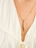Model in a white top wearing a long twisting gold-tone bar pendant on a fine snake chain