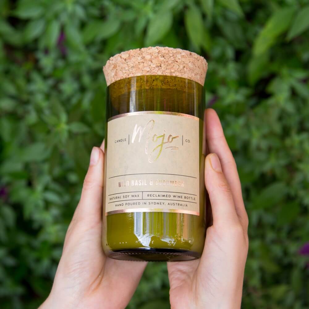 Hands holding the Wild Basil & Cucumber candle in its green reclaimed wine bottle in a garden