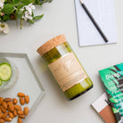 Wild Basil & Cucumber candle lying flat with almonds, a notebook and magazines