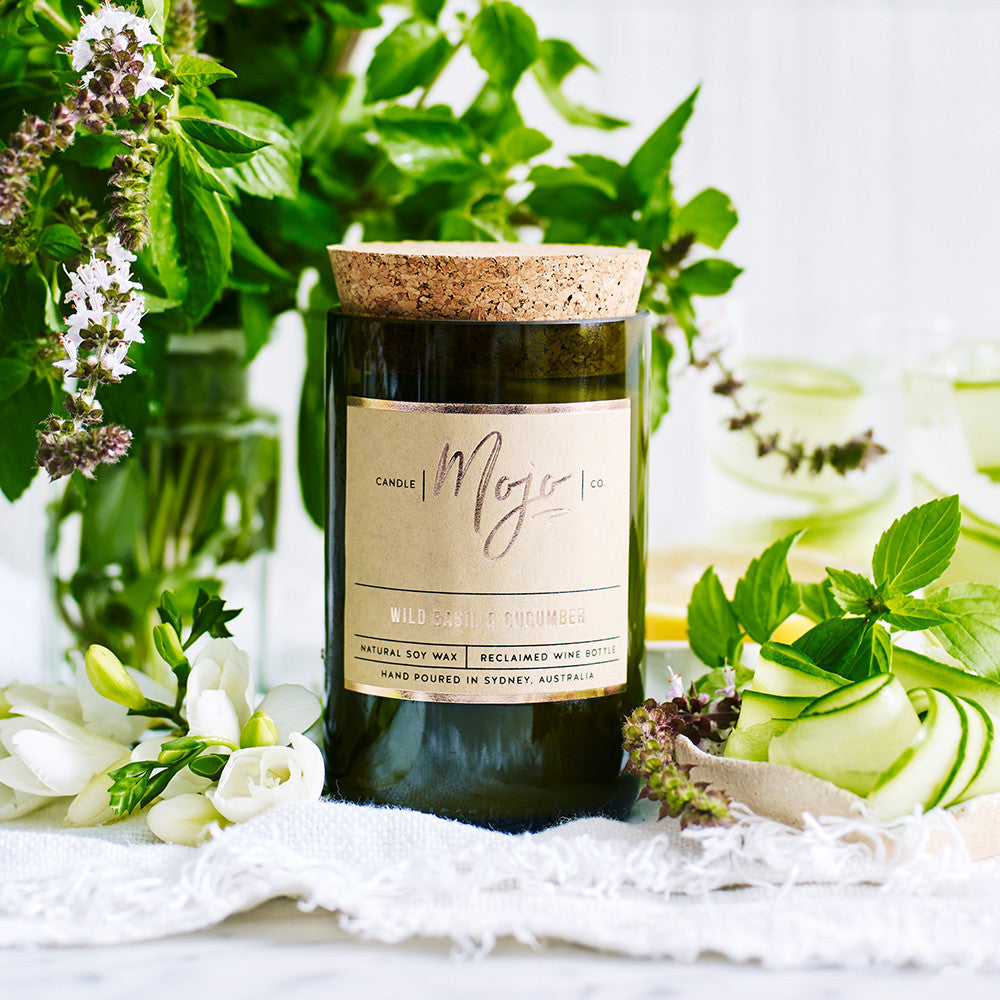 Wild Basil & Cucumber candle in a green reclaimed wine bottle among flowering basil and greenery