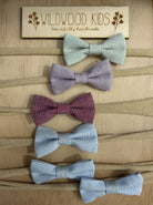 Six Wildwood Kids baby headbands on a timber board, with fabric bows in mint, lilac, berry and pale blue on soft beige stretch bands