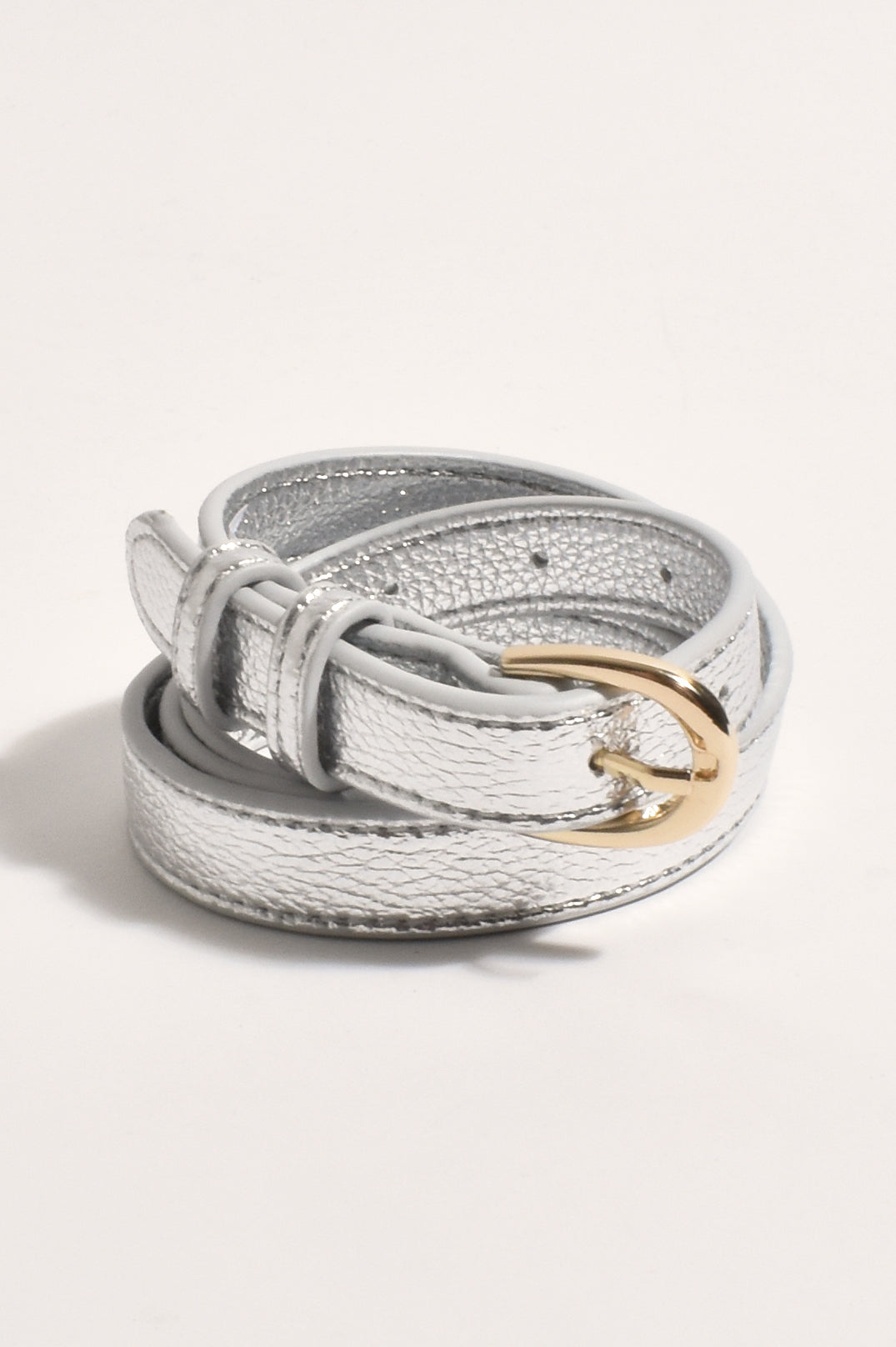 Thin metallic silver belt coiled up, showing its rounded gold-tone buckle