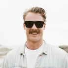 A man with a moustache wearing the Dalton sunglasses outdoors, front on