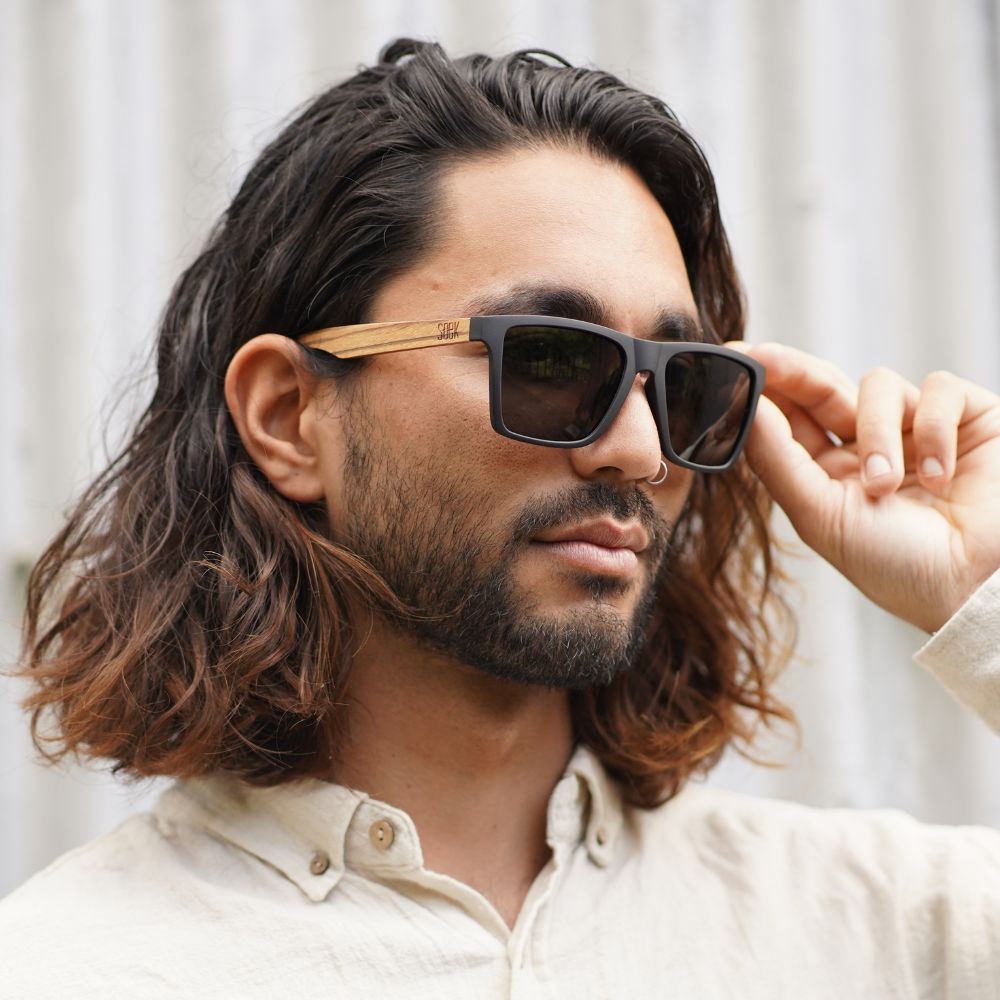 A man with long dark hair adjusting the Dalton sunglasses as he wears them