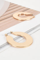 Pair of flat gold-tone crescent hoop earrings on a white and blush ribbed surface