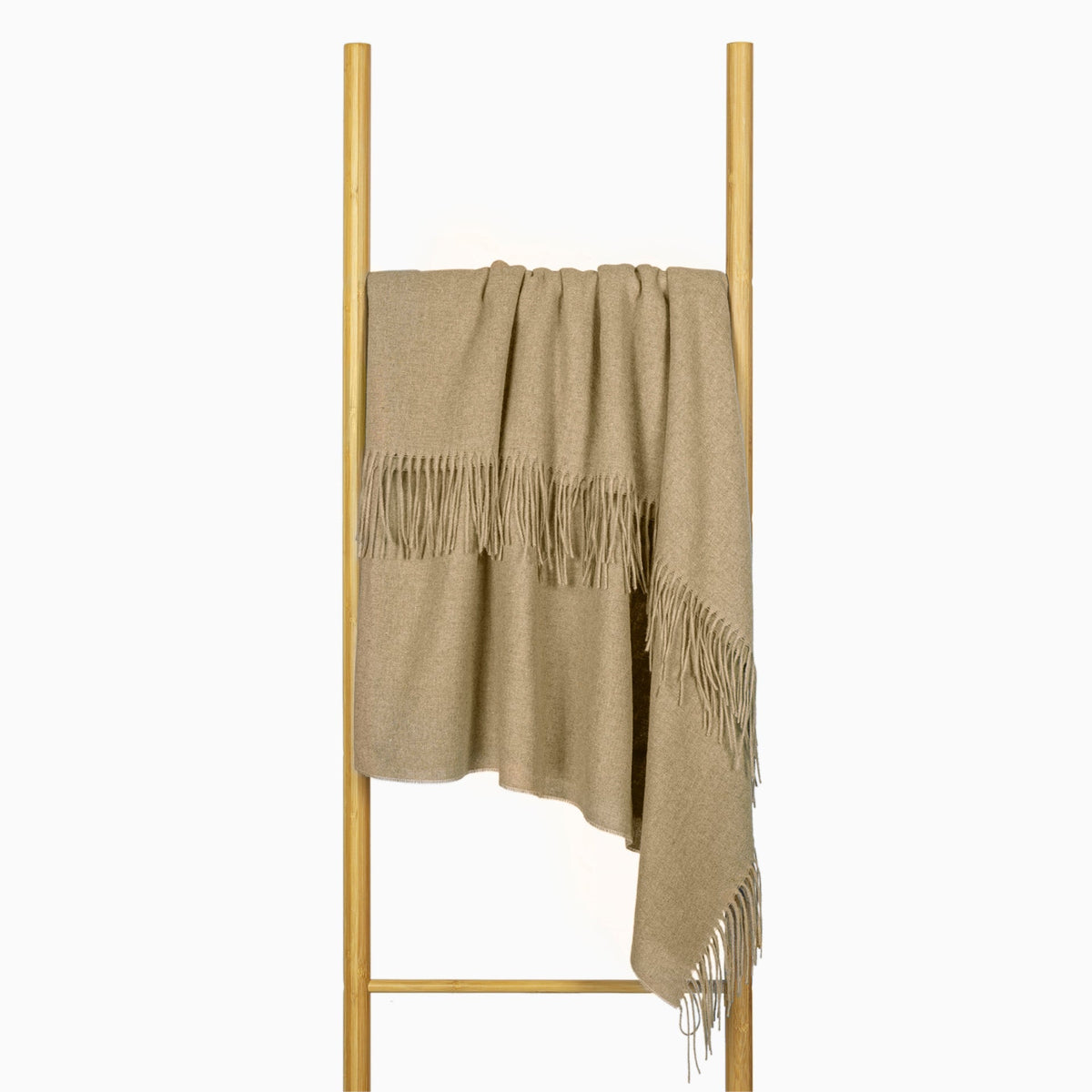 Camel fringed throw draped over a timber ladder rail against a white wall