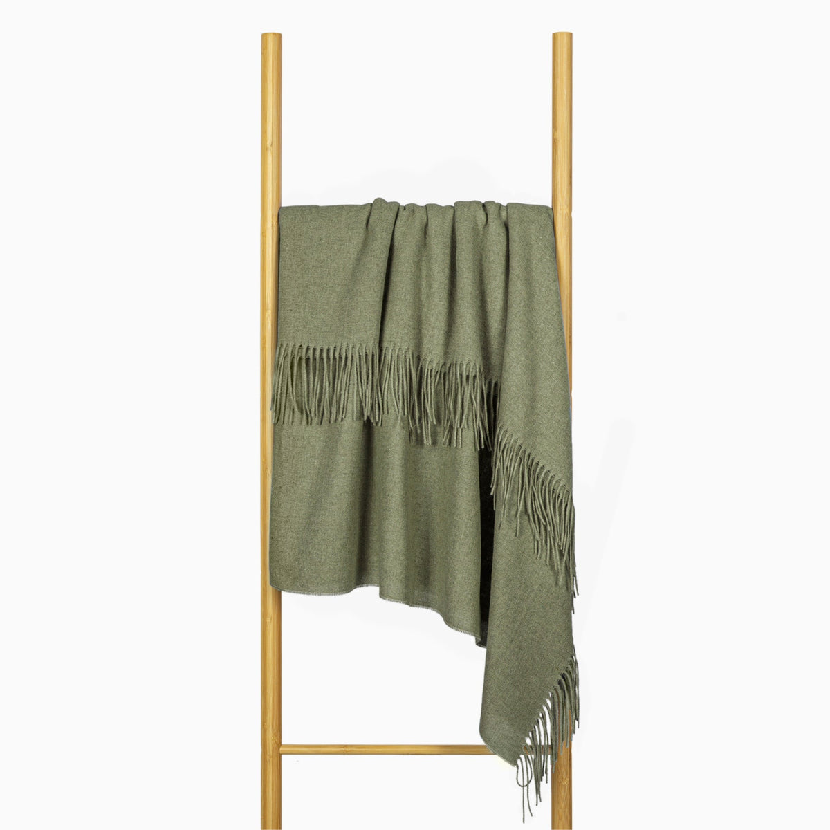 Olive fringed throw hung over a timber ladder rail against a white wall