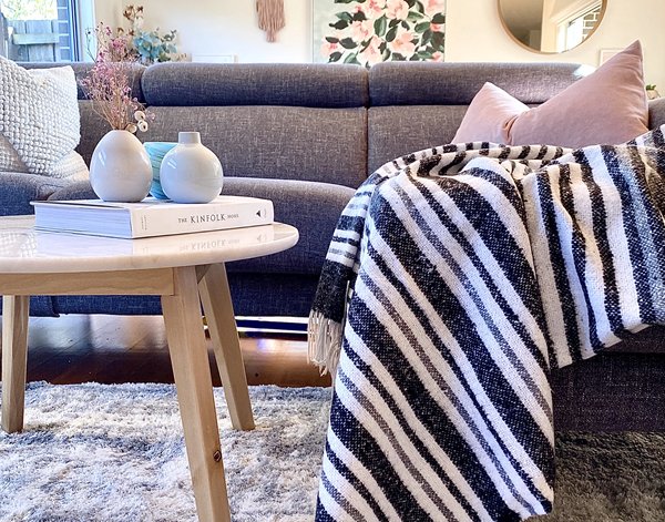 Striped monochrome throw draped over a dark lounge in a styled living room with a timber coffee table