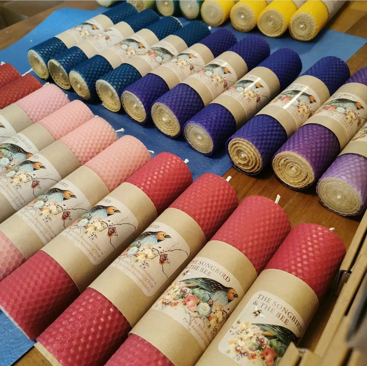 Rows of hand-rolled beeswax pillar candles in red, pink, purple, navy and yellow with Songbird and the Bee kraft labels