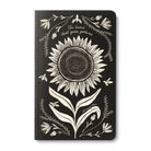 Black journal cover with a white line-drawn sunflower and the words the heart that gives, gathers