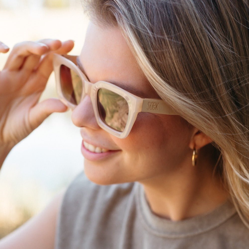 A woman with blonde hair lifting the Zahra sunglasses, worn outdoors