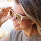 A woman with blonde hair lifting the Zahra sunglasses, worn outdoors
