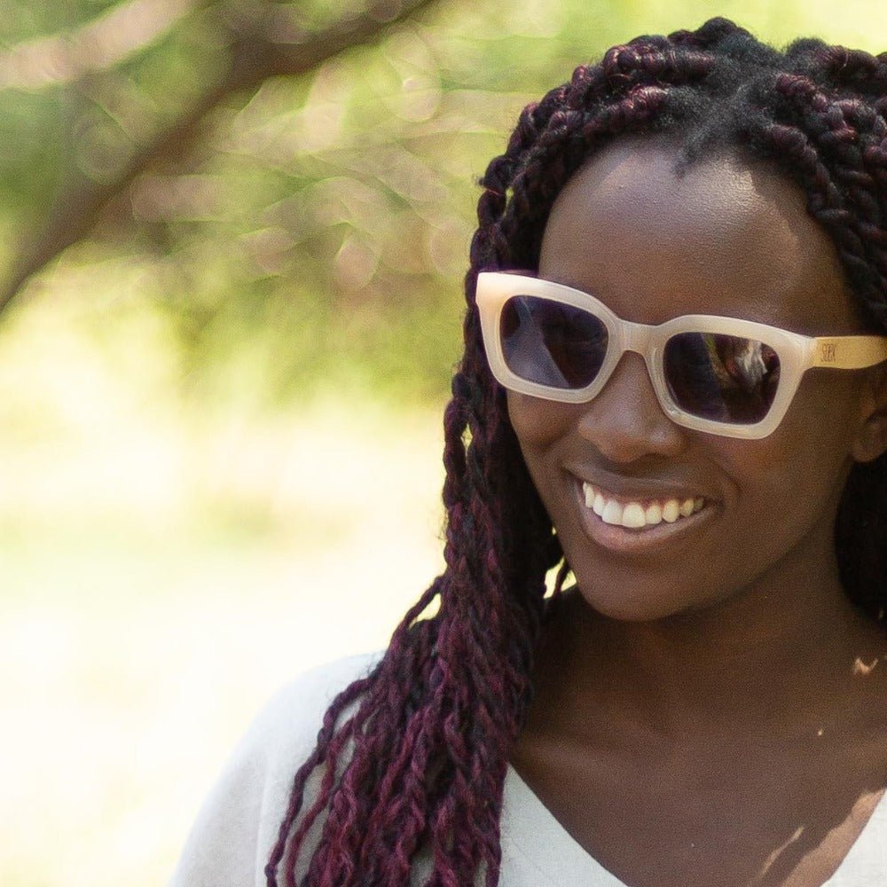 A woman with braided hair smiling outdoors, wearing the Zahra sunglasses