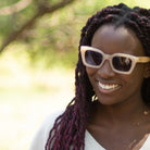 A woman with braided hair smiling outdoors, wearing the Zahra sunglasses